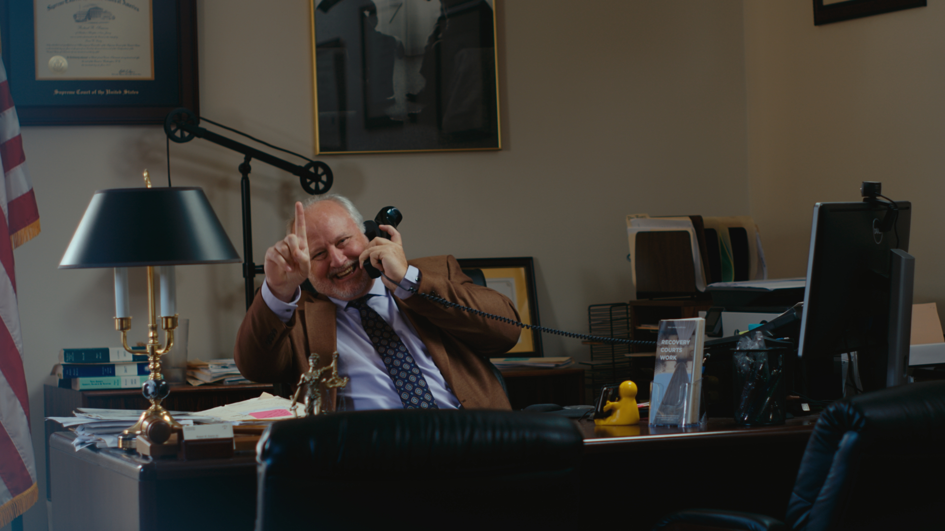 A man in a suit laughing on the phone inside an office
