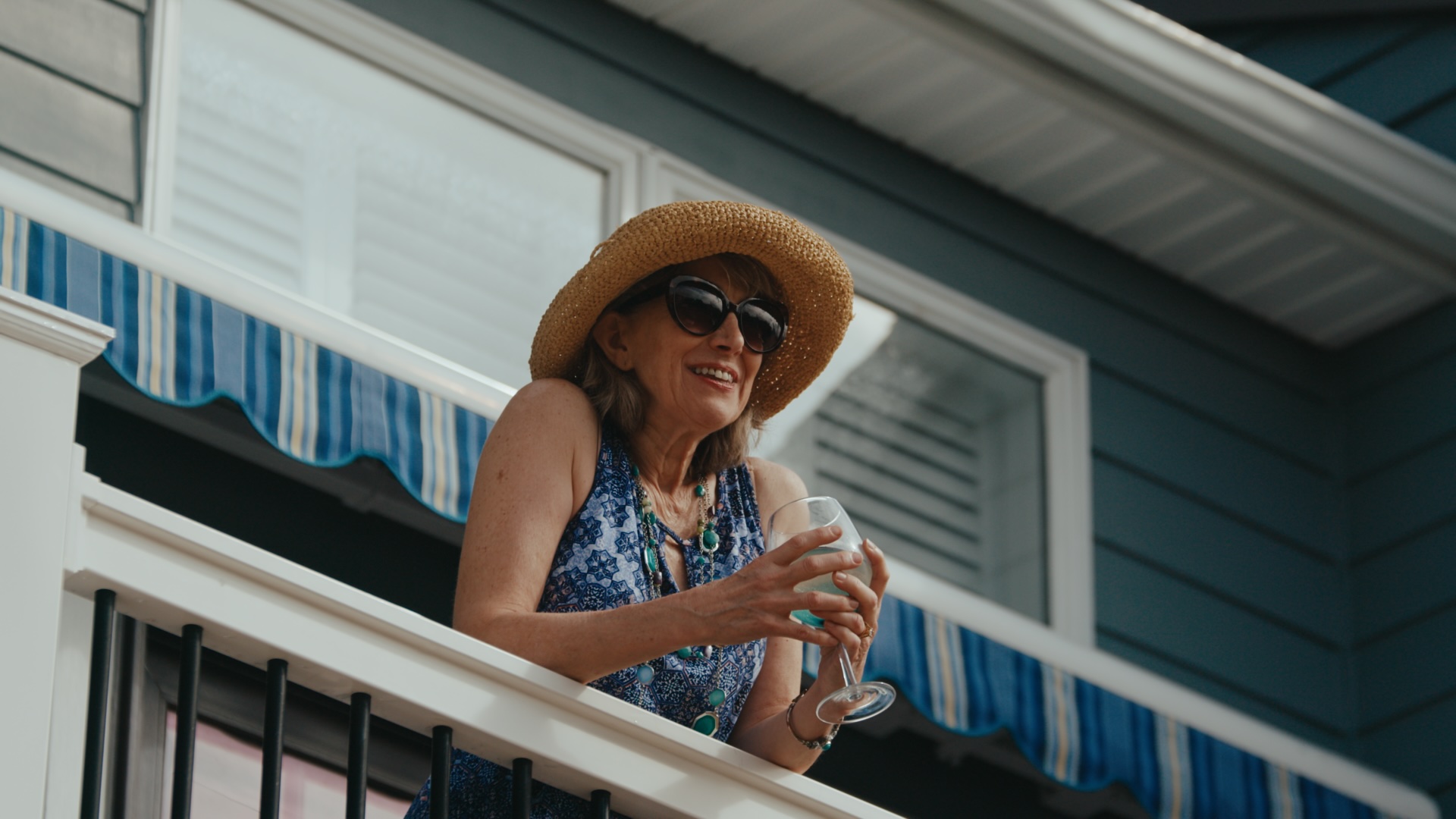A woman in a sunhat with a glass of wine on a beach house balcony