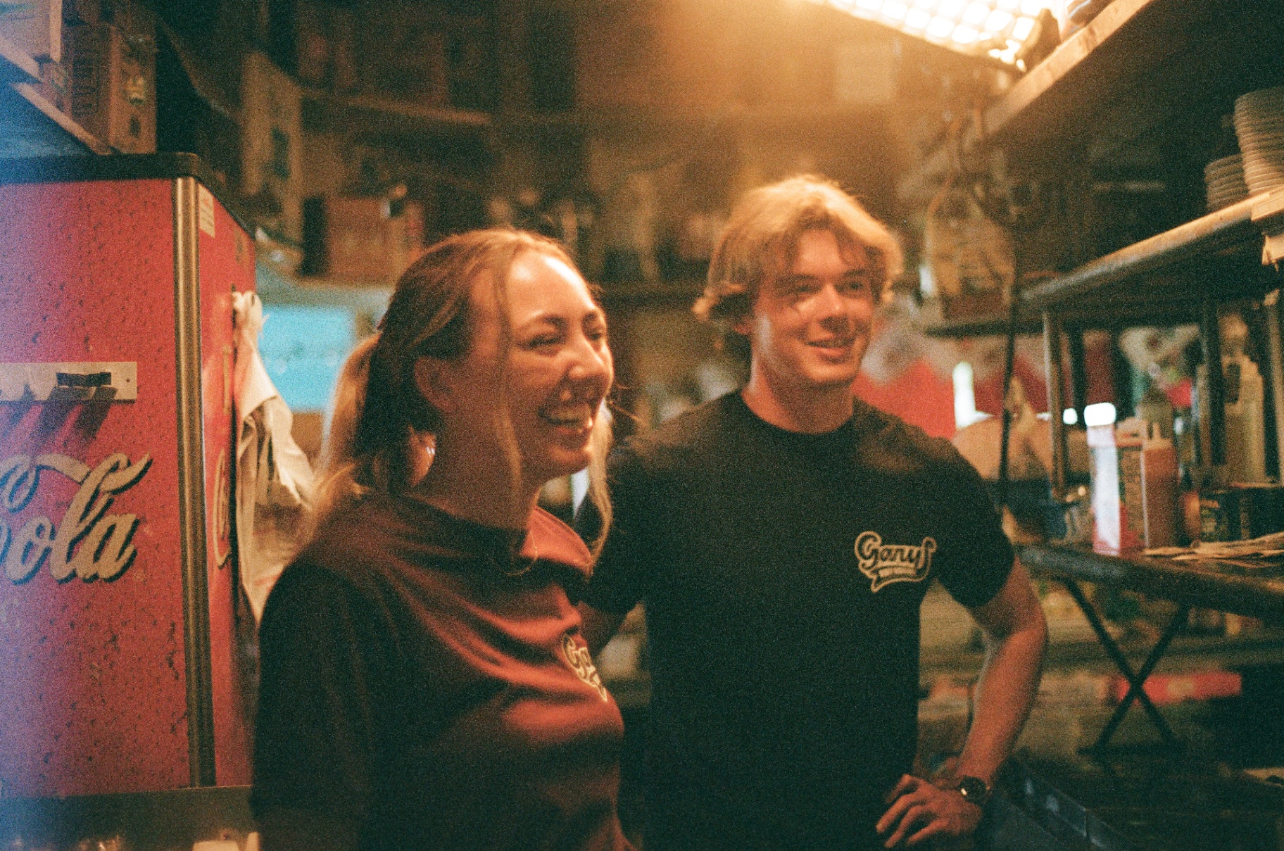 Two crew members laughing behind the bar at Gary’s, bathed in warm light.